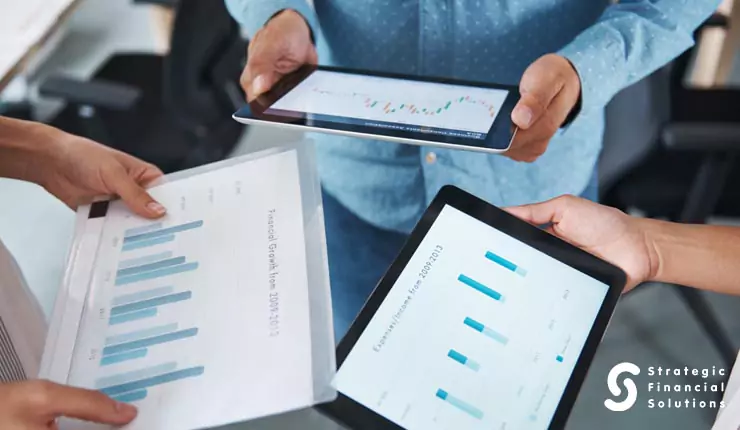 financial-advisor-payment-models People comparing financial charts displayed on tablets and printed documents.