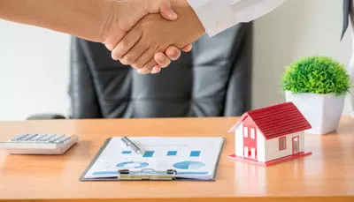 superannuation-estate-planning-advice Adviser and client shaking hands beside financial documents and a model house.