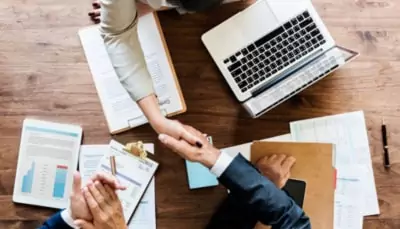 superannuation-investment-advice-meeting Adviser and client shaking hands after reviewing investment documents at a desk.