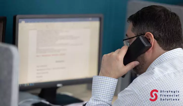 types-of-financial-advisory-services Financial adviser speaking with a client by phone while working at a computer.